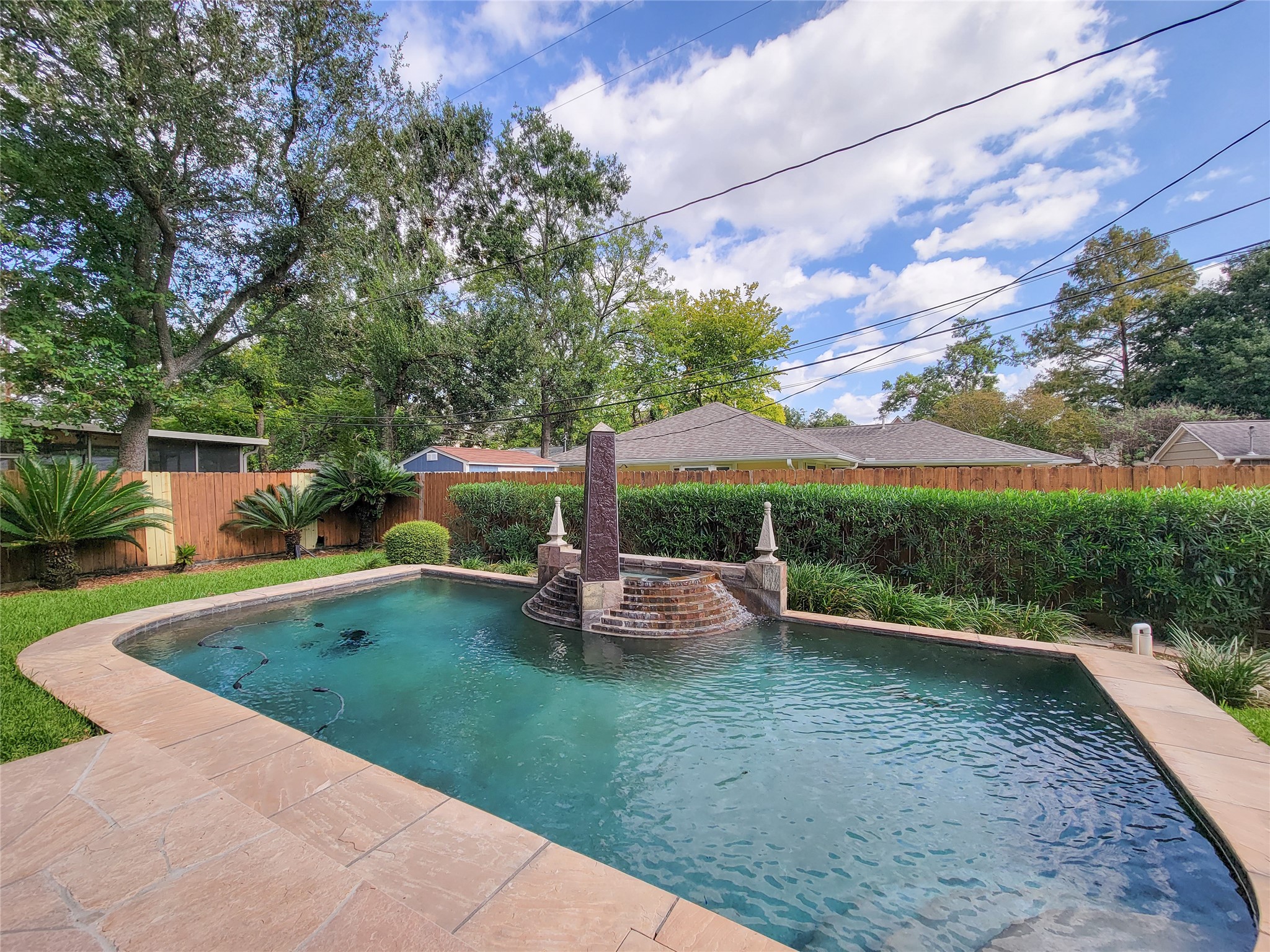 1118 Colonial Street Bellaire, TX 77401 - Photo 41 of 50 This backyard features a serene pool with a central waterfall feature, surrounded by lovely landscaping and a wooden fence, offering privacy and a peaceful retreat.
