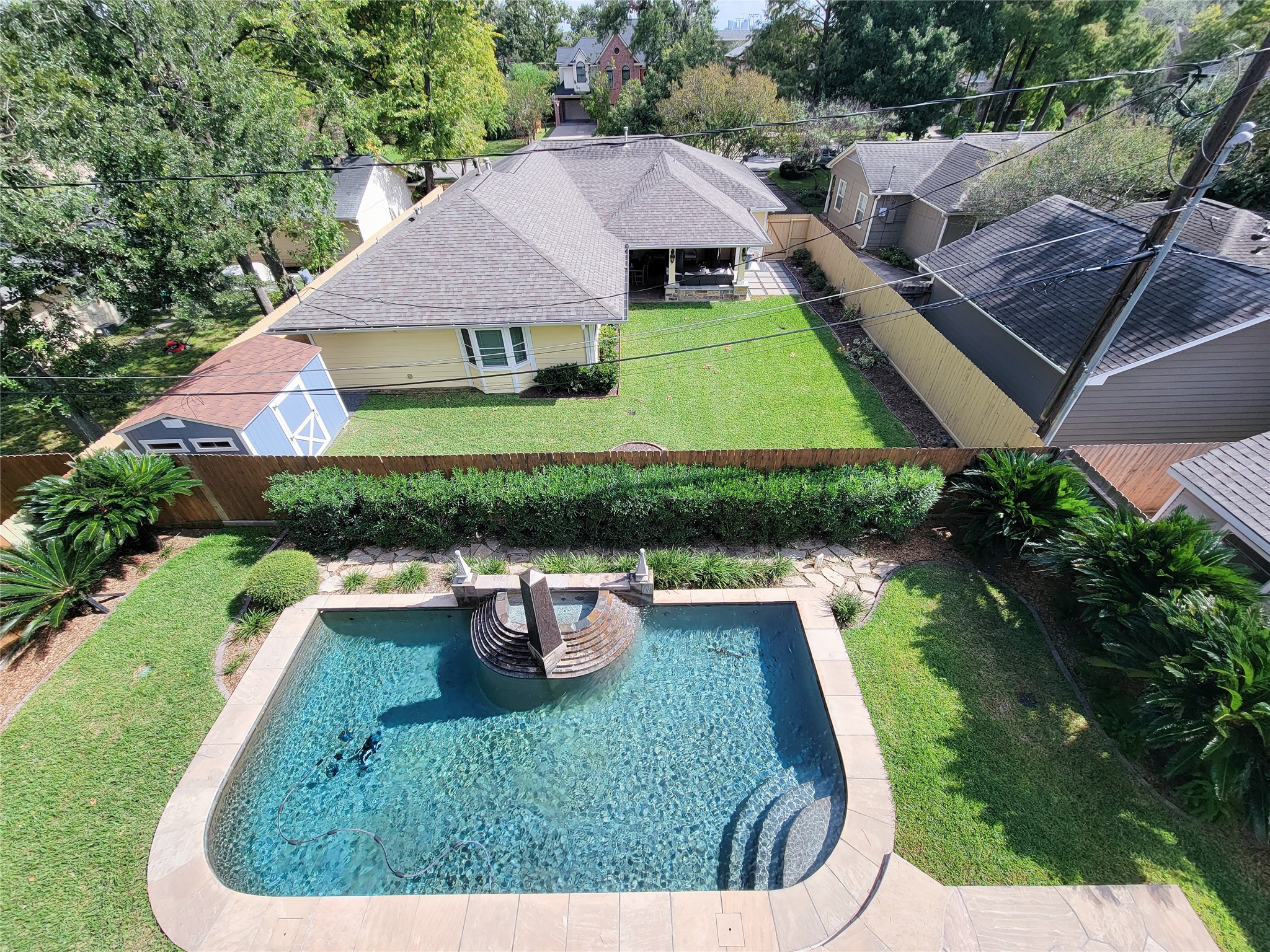 1118 Colonial Street Bellaire, TX 77401 - Photo 42 of 50 This view from the third-floor balcony showcases a spacious backyard featuring a well-maintained lawn, a pool with a decorative water feature, and surrounding greenery.