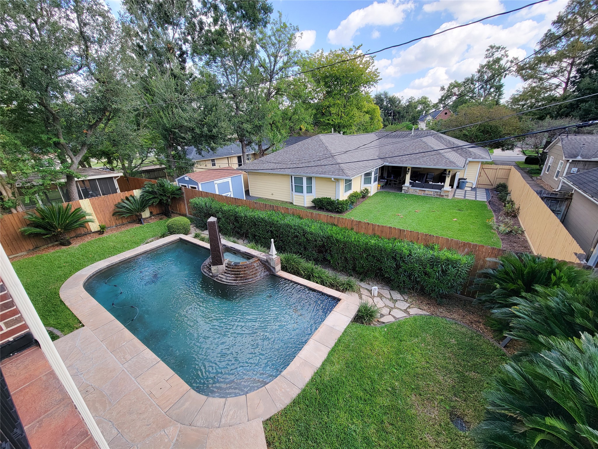 1118 Colonial Street Bellaire, TX 77401 - Photo 43 of 50 Lush landscaping, wooden fence, and in-ground swimming pool with a water feature. The house has a covered patio area, surrounded by mature trees. Perfect for outdoor relaxation and entertaining.