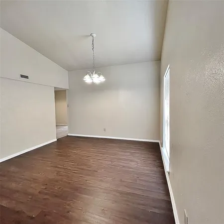 a view of an empty room with wooden floor and chandelier