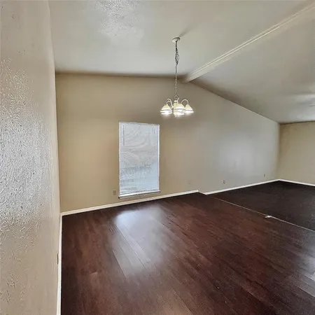 an empty room with wooden floor chandelier and windows