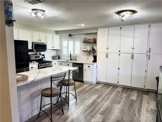 a kitchen with stainless steel appliances a refrigerator a stove a sink dishwasher and white cabinets with wooden floor
