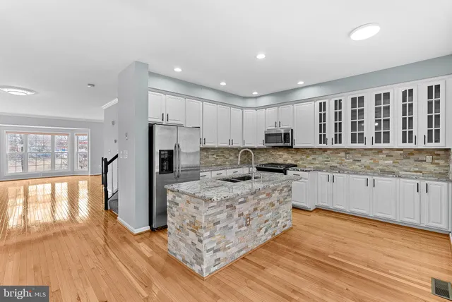 a kitchen with stainless steel appliances granite countertop a stove top oven a sink dishwasher a refrigerator and white cabinets with wooden floor