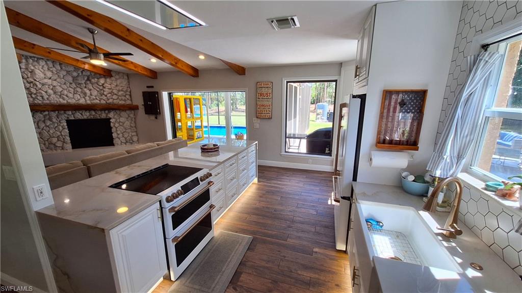 3690 27th Avenue Southwest Naples, FL 34117 - Photo 11 of 32 Kitchen with range with two ovens, dark wood finished floors, beam ceiling, white cabinets, and freestanding refrigerator