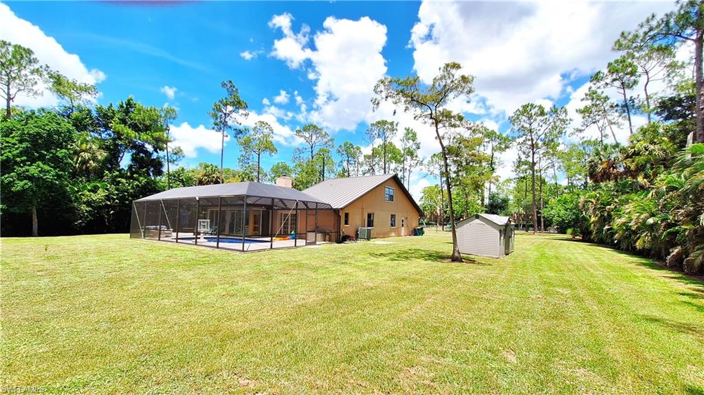 3690 27th Avenue Southwest Naples, FL 34117 - Photo 6 of 32 View of green lawn featuring a lanai, a swimming pool, a shed, and view of wooded area