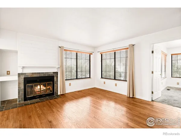 a view of an empty room with wooden floor fireplace and a window