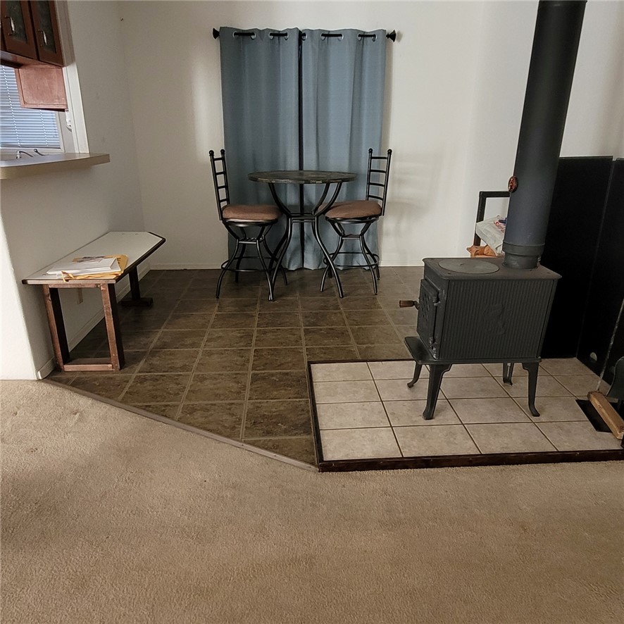 9732 2nd Street Chloride, AZ 86431 - Photo 13 of 28 This area features a wood-burning stove on a tiled hearth, with durable tile flooring extending towards a window with blinds and blue curtains