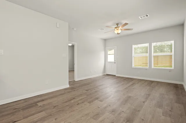 an empty room with wooden floor chandelier fan and windows