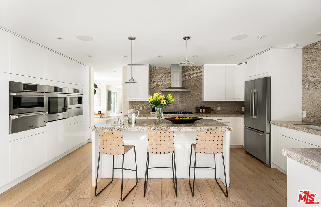 1600 North Kings Road Los Angeles, CA 90069 - Photo 14 of 37 a kitchen with stainless steel appliances kitchen island granite countertop a refrigerator a stove a sink a dining table and chairs with wooden floor