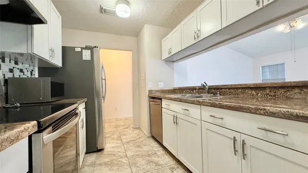 a large white kitchen with granite countertop a sink and dishwasher a stove top oven with wooden floor