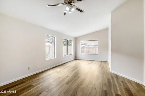 an empty room with wooden floor chandelier fan and windows