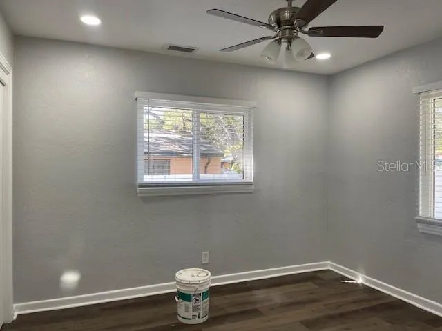 a view of an empty room with wooden floor and fan