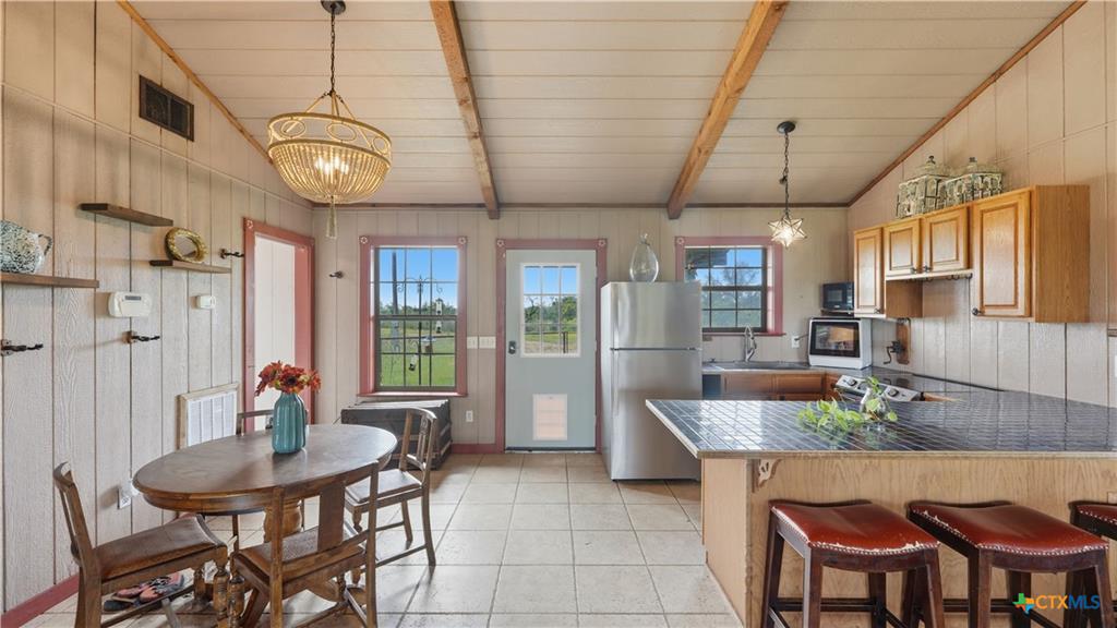 127 Offer Llano, TX 78643 - Photo 3 of 40 Kitchen and dining area featuring vaulted ceilings with exposed wood beams, a breakfast bar with dark countertops, wood-finish cabinetry, and ceramic tile flooring