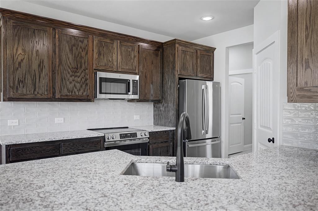 44 Karol Jean Way Quinlan, TX 75474 - Photo 12 of 36 Kitchen featuring dark wood finish cabinetry, stainless steel appliances, light stone counters, and tasteful backsplash