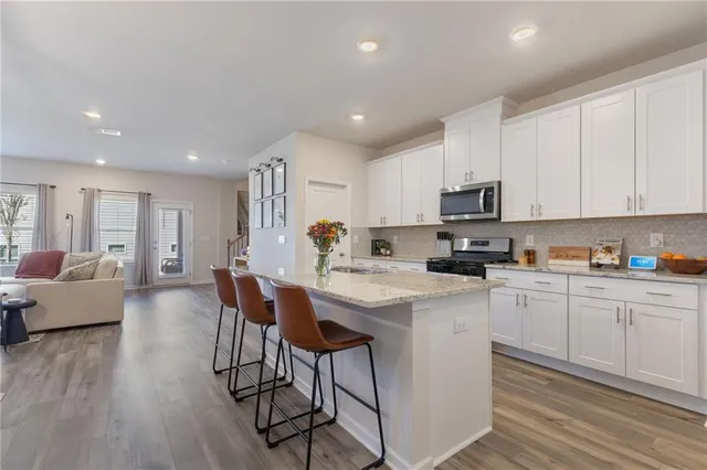 a kitchen with stainless steel appliances granite countertop a refrigerator a stove top oven a sink dishwasher and white cabinets with wooden floor
