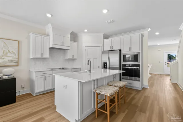 a kitchen with stainless steel appliances a sink a stove a refrigerator cabinets and a wooden floor