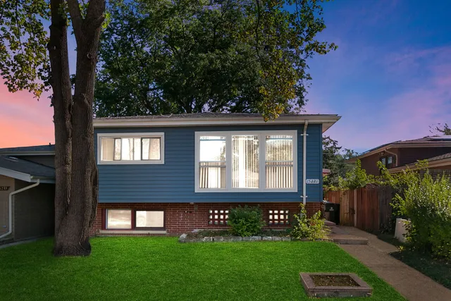 a view of a brick house with a yard potted plants and large tree