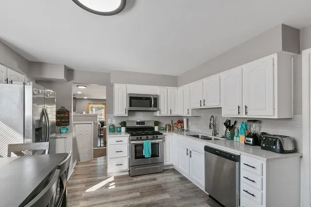 a kitchen with stainless steel appliances granite countertop a stove top oven a sink dishwasher and a refrigerator with white cabinets