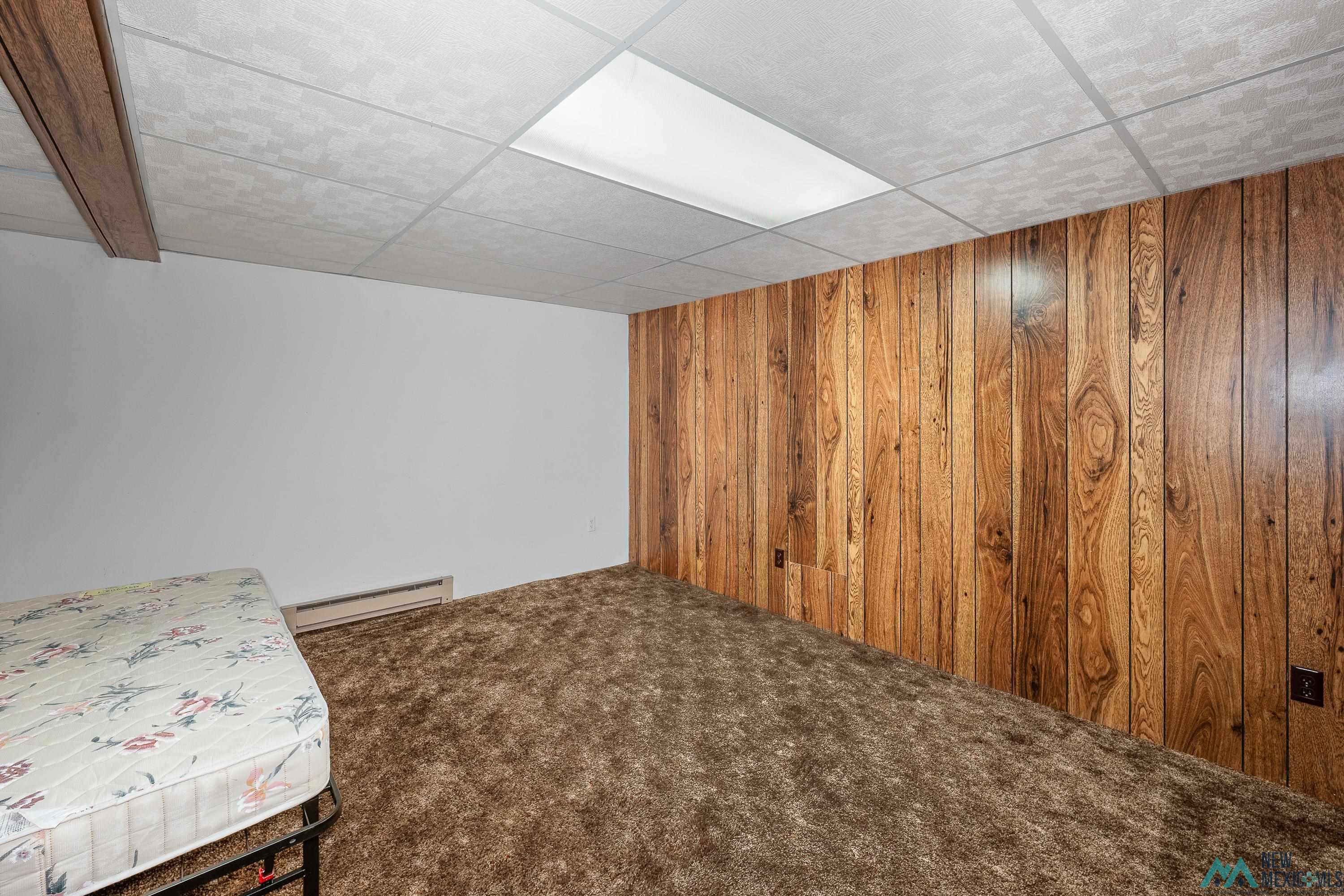727 South 6th Street Raton, NM 87740 - Photo 20 of 47 Unfurnished bedroom with carpet, wooden walls, baseboard heating, and a drop ceiling