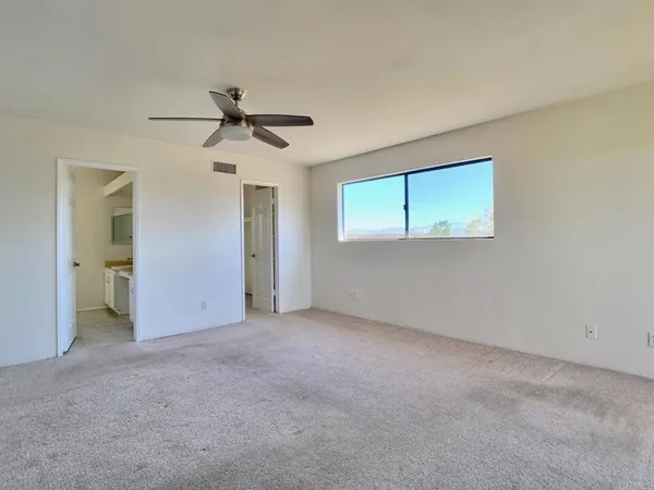 an empty room with chandelier fan and windows