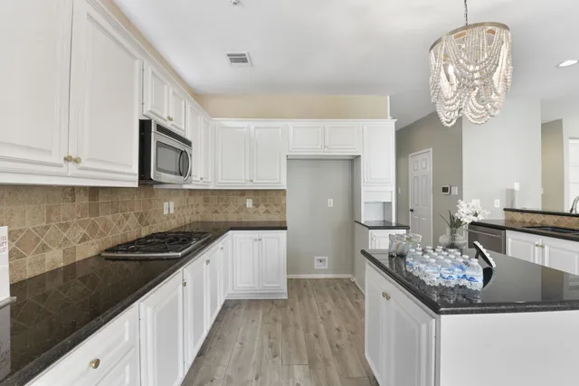 a kitchen with stainless steel appliances kitchen island granite countertop a refrigerator a stove a sink and white cabinets with wooden floor