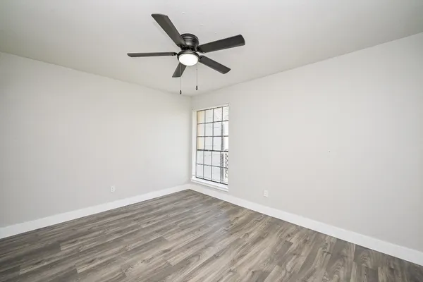 an empty room with wooden floor fan and windows