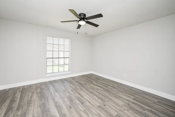 an empty room with wooden floor fan and windows