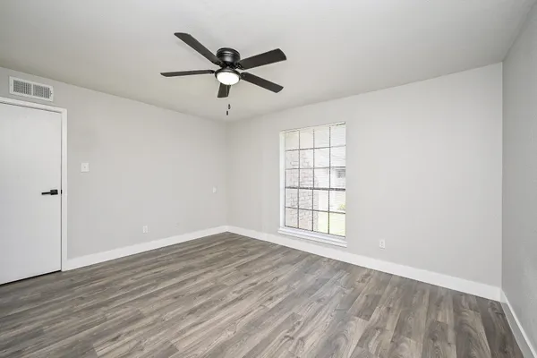 an empty room with wooden floor fan and windows