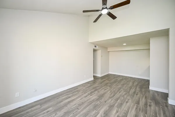 an empty room with wooden floor ceiling fan and windows
