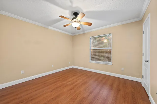 an empty room with wooden floor chandelier fan and windows