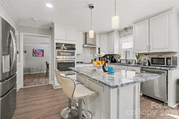 a kitchen with stainless steel appliances granite countertop a sink a stove a refrigerator cabinets and chairs