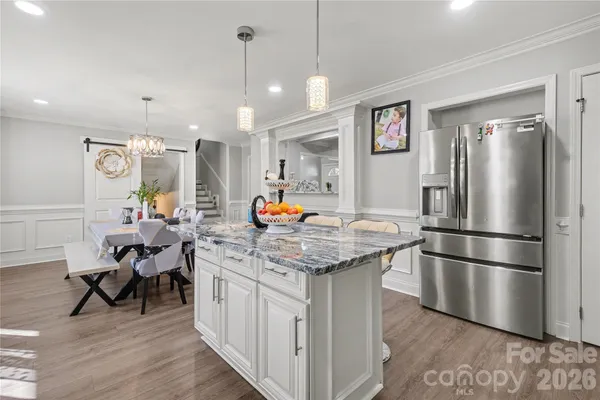 a kitchen with stainless steel appliances granite countertop a refrigerator a sink dishwasher a dining table and chairs with wooden floor