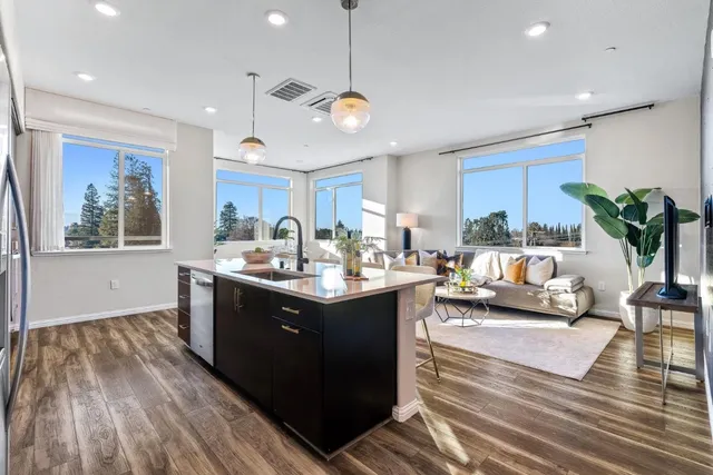 a kitchen with stainless steel appliances granite countertop a sink dishwasher a refrigerator and a dining table with wooden floor