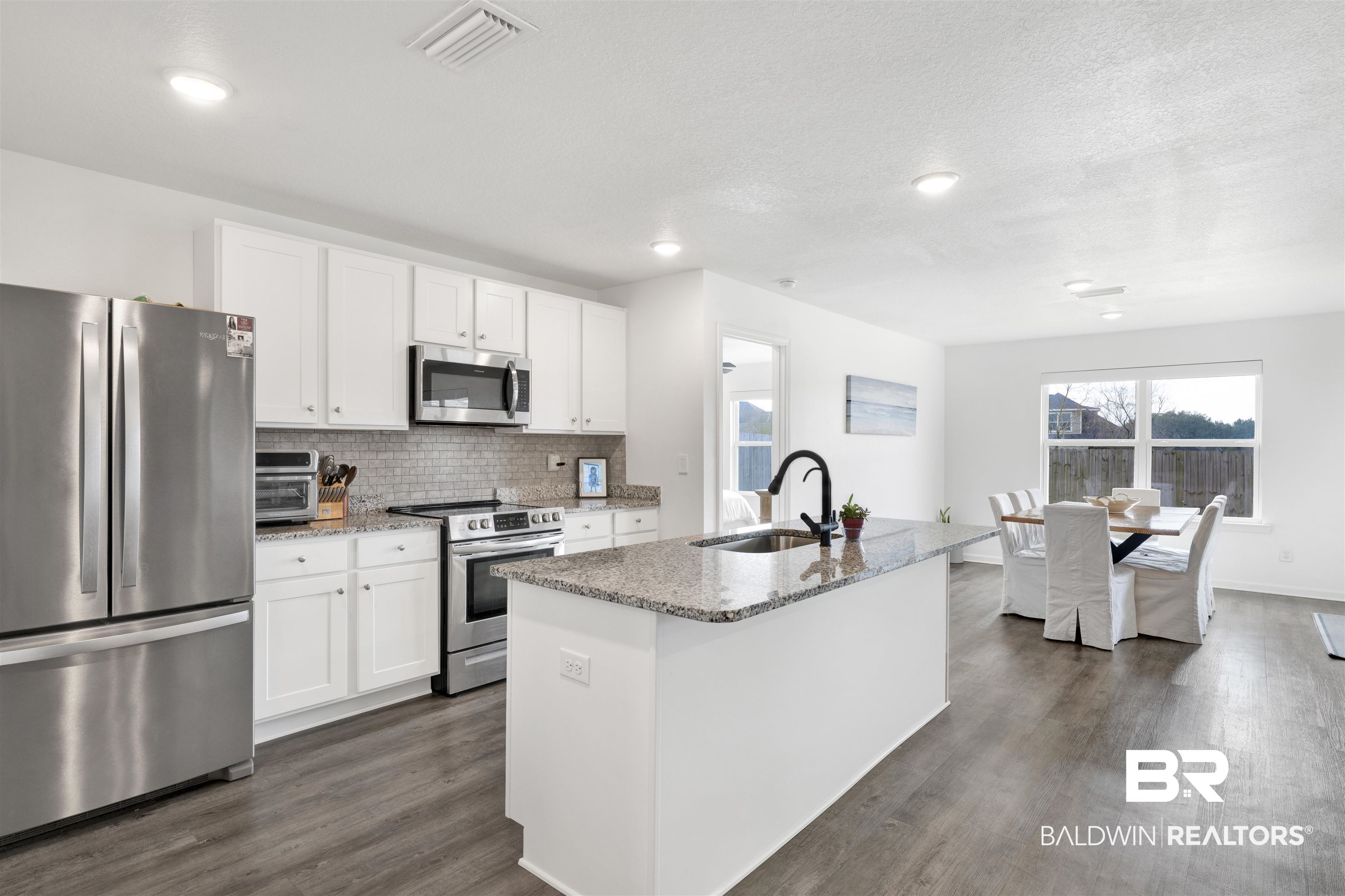 10763 Paget Drive North Mobile, AL 36608 - Photo 5 of 24 Kitchen featuring stainless steel appliances, light stone countertops, a center island with sink, dark wood-style floors, and white cabinets