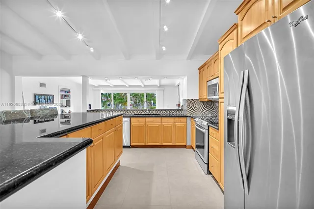 a large kitchen with stainless steel appliances granite countertop a refrigerator a sink dishwasher a stove and white countertops with wooden floor