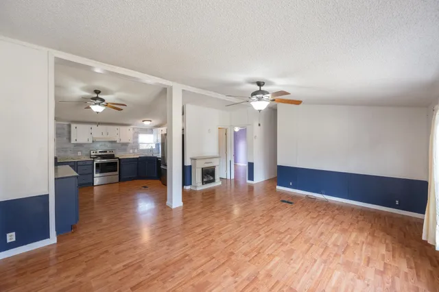 a view of an empty room with wooden floor and a kitchen