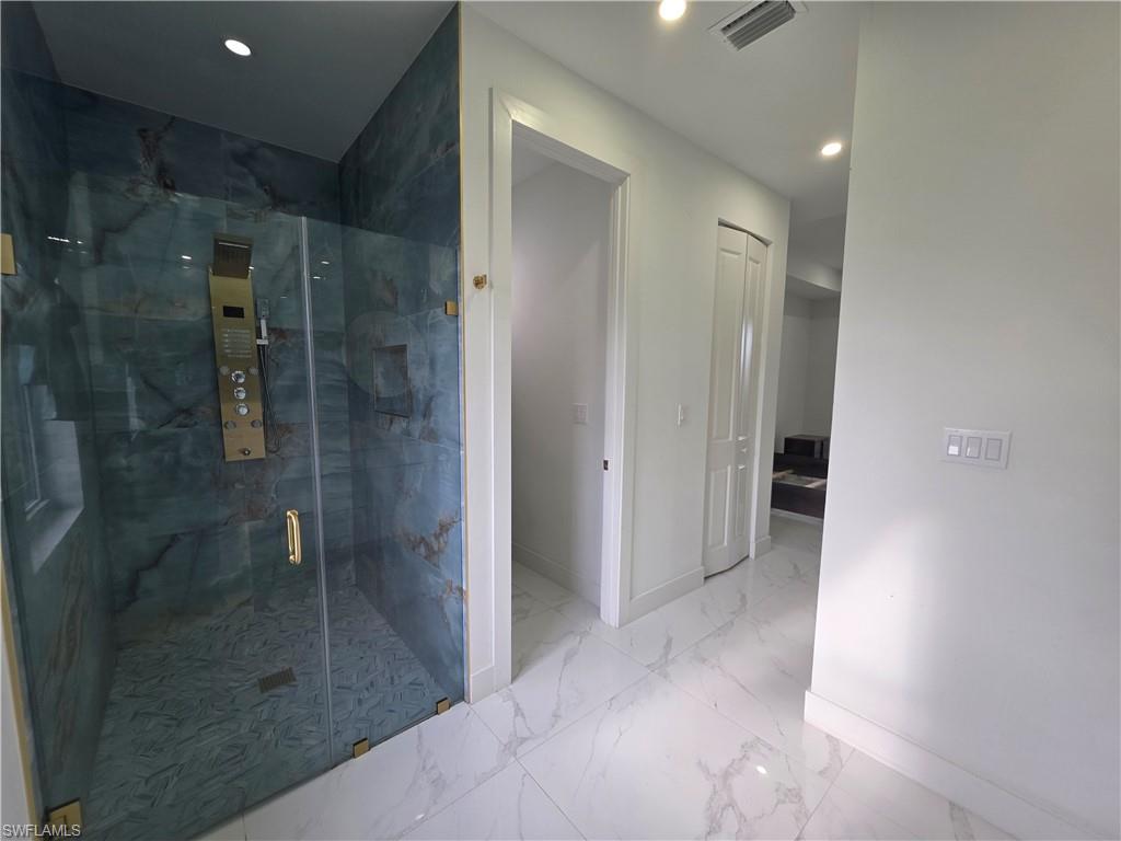 331 Nelson Road North Cape Coral, FL 33993 - Photo 23 of 29 Glass-enclosed shower featuring blue-toned stone walls with natural veining, a patterned floor, recessed shelving, and a gold-finish multi-function shower panel