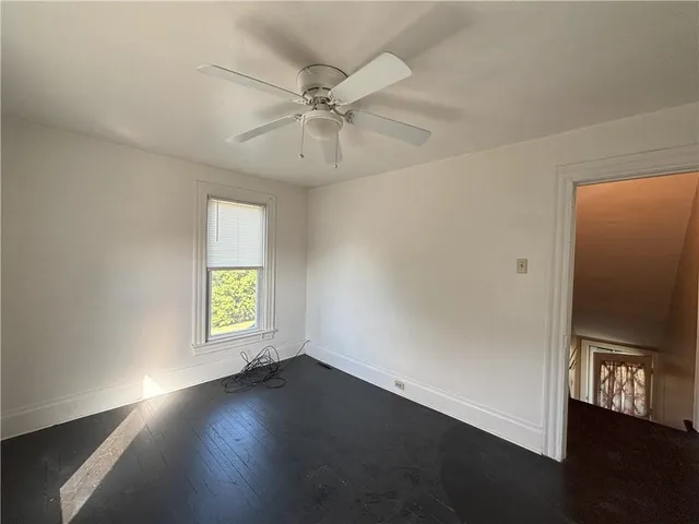 an empty room with wooden floor fan and windows