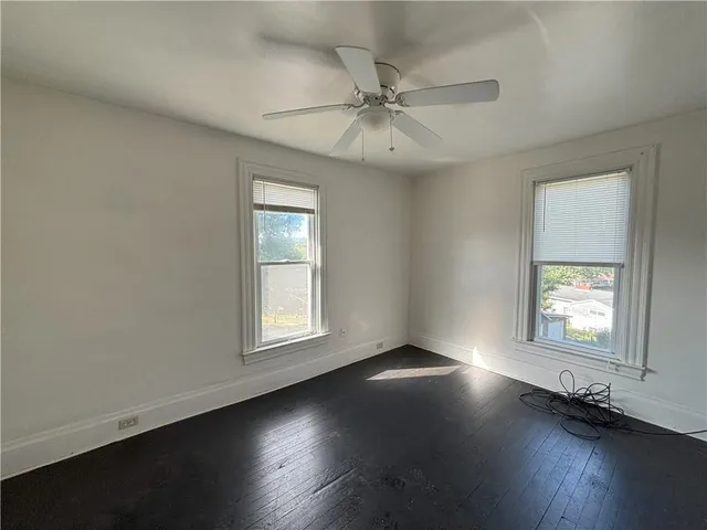 an empty room with wooden floor windows and fan