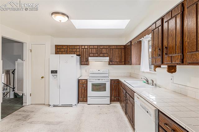 1653 Cragin Road Colorado Springs, CO 80920 - Photo 7 of 27 Kitchen with white appliances, tile counters, a skylight, dark brown cabinets, and under cabinet range hood