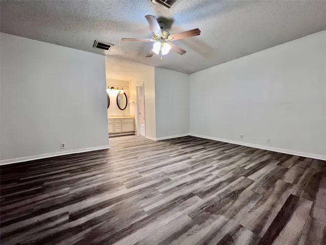 a view of an empty room with wooden floor and a ceiling fan