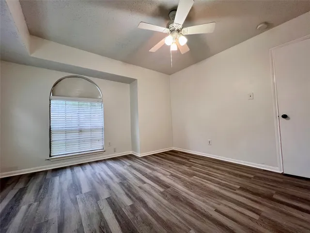 an empty room with wooden floor chandelier fan and windows