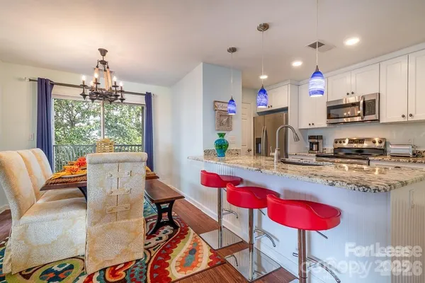 a kitchen with stainless steel appliances kitchen island granite countertop a dining table chairs stove and white cabinets