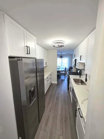 a kitchen with stainless steel appliances granite countertop a refrigerator a sink dishwasher a stove and white countertops with wooden floor