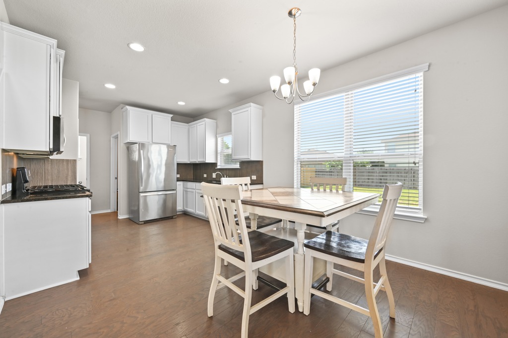 209 Noddy Road Buda, TX 78610 - Photo 8 of 27 Warm wood flooring and classic crown molding frame a sunlit dining area next to the kitchen.