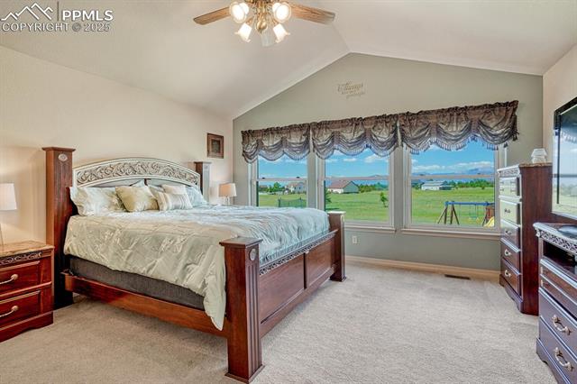 11455 Dallas Road Peyton, CO 80831 - Photo 25 of 50 Vaulted Main Level Primary Bedroom with neutral carpet, lighted ceiling fan, and beautiful mountain views from the wall of windows.