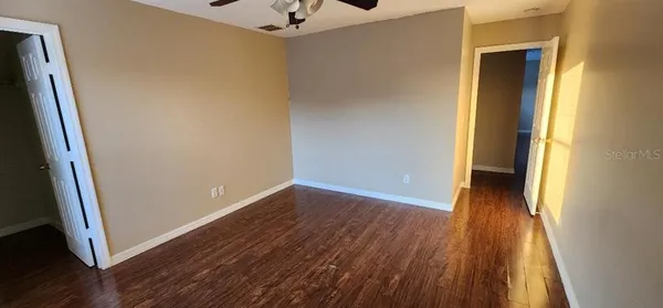 an empty room with wooden floor chandelier fan and windows