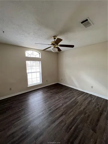 an empty room with wooden floor a ceiling fan and windows