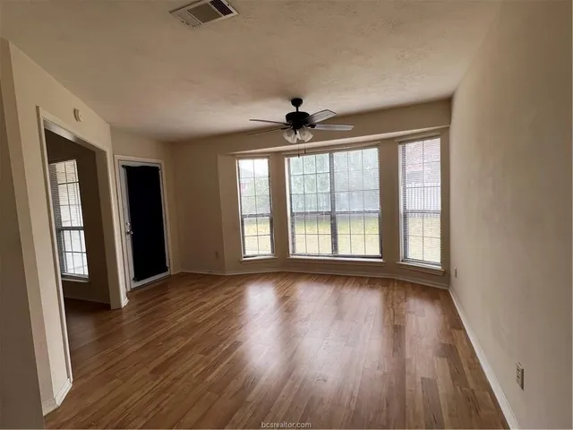 a view of an empty room with wooden floor and a window