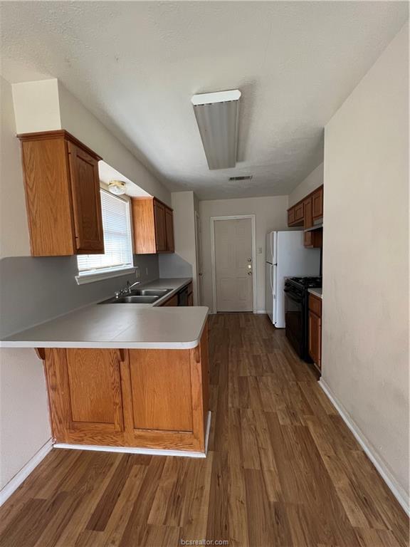 4611 Brompton Lane Bryan, TX 77802 - Photo 8 of 18 Kitchen with brown cabinets, a peninsula, light countertops, dark wood-type flooring, and a textured ceiling